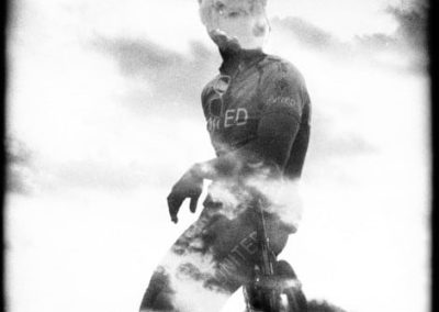 Double-exposure, in black and white, of a cyclist and clouds.
