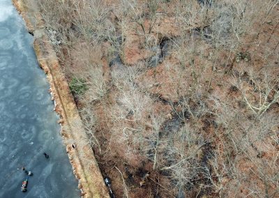 An aerial view in winter of Lake Hudsonia dam next to the dark blue frozen pond.