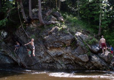 Young people play in a swimming hole, with rope swing, in Vermont
