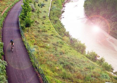 A solitary cyclist on a bike path between a field and a river in the early morning.