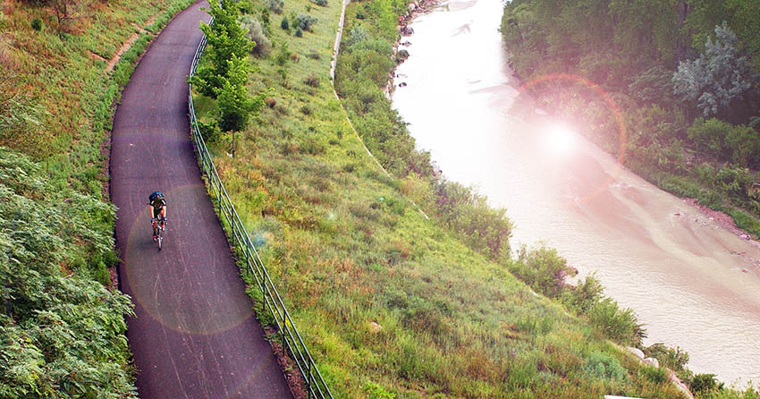 A solitary cyclist on a bike path between a field and a river in the early morning.