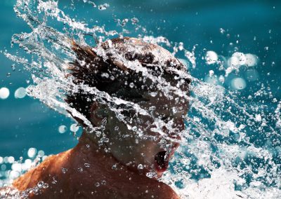 a close up of a young boy tossing water from his hair in a public swimming pool