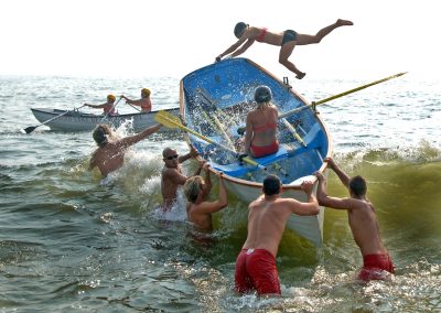 lifeguards control a lifesaver boat as one lifeguard struggles to hang on