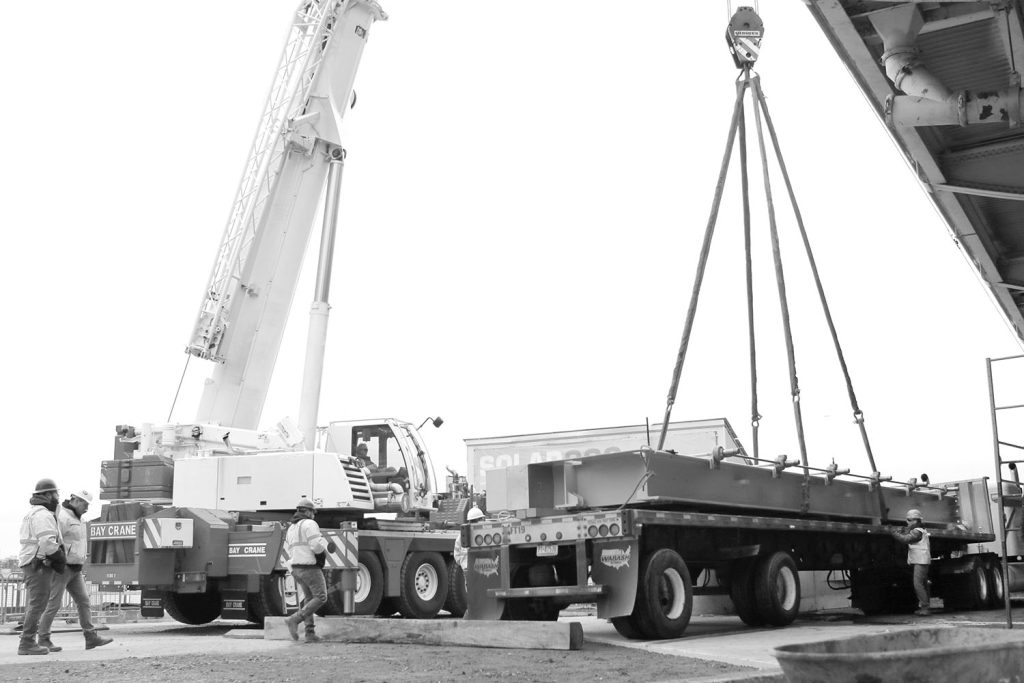 a crane and rigging prepare to hoist a massive steel gate in a black and white picture