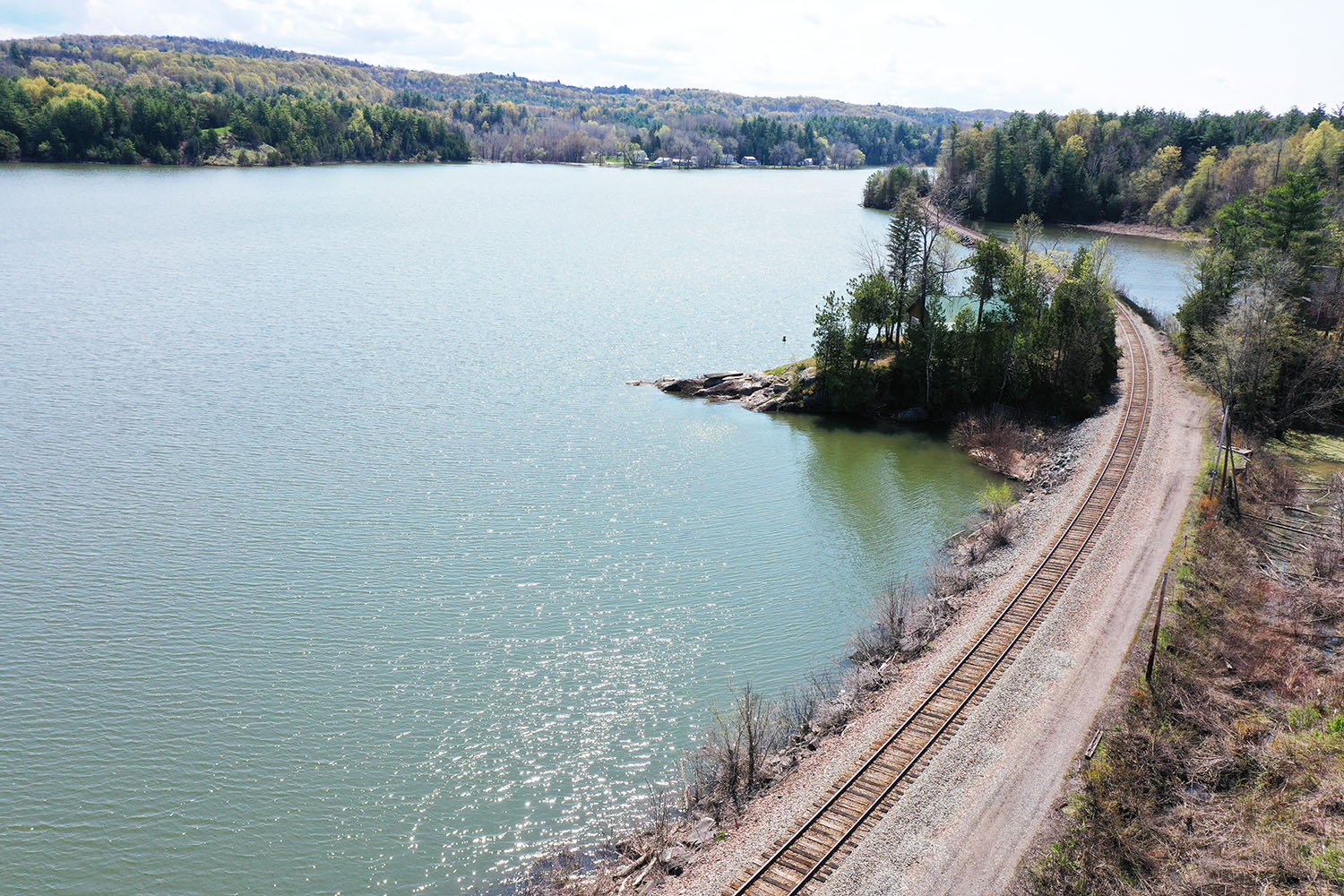 Aerial view of Lake Champlain with railroad tracks in foreground, blue lake and mountains in background