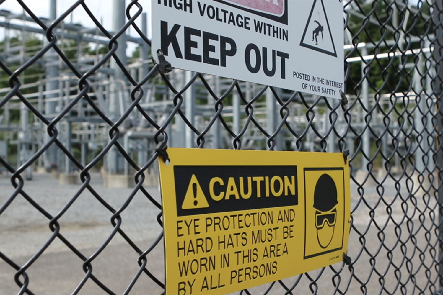 Close up view of chain link fence and warning signs around substation.