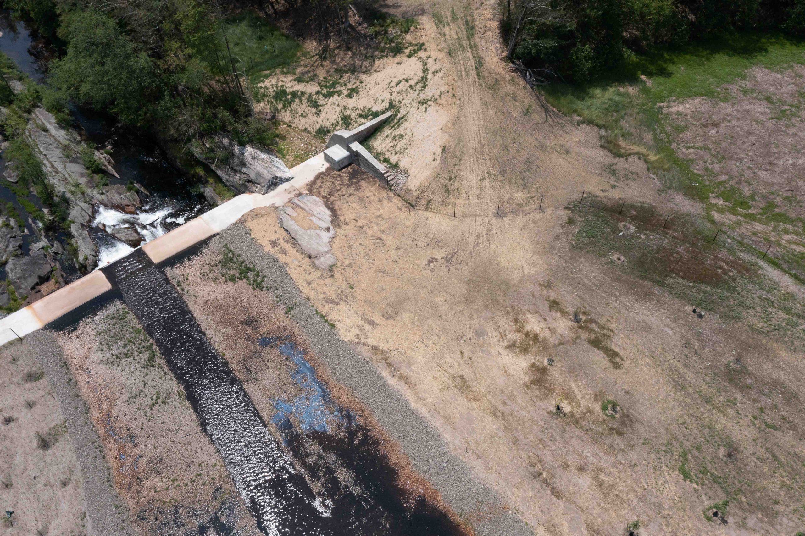 An aerial view of a dam and stream, with sparse vegetation